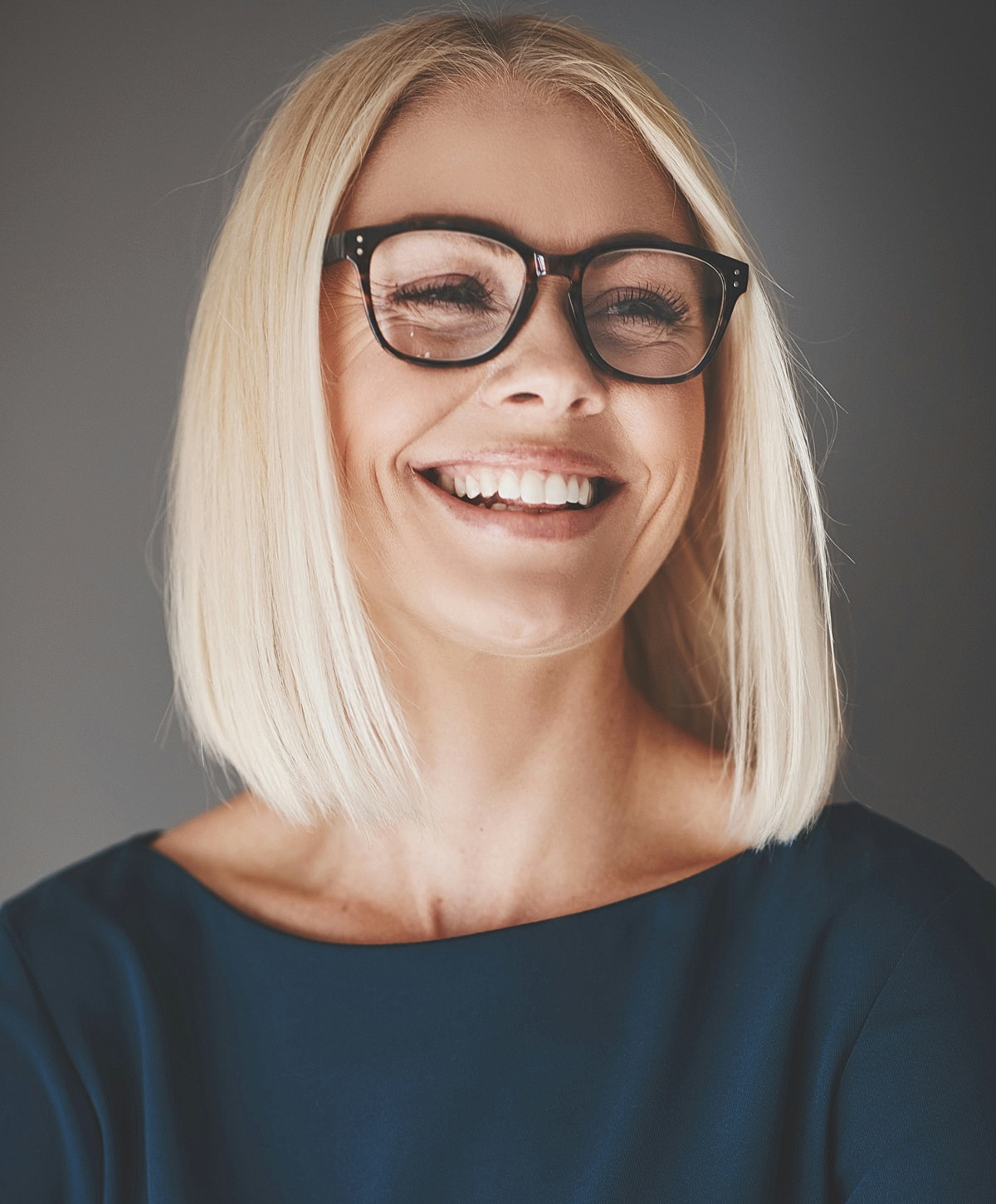 Smiling woman with glasses and short blonde hair.