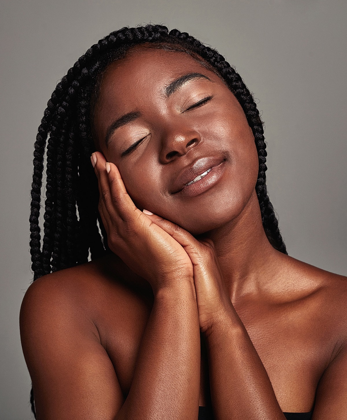 Smiling woman with braided hair, eyes closed.