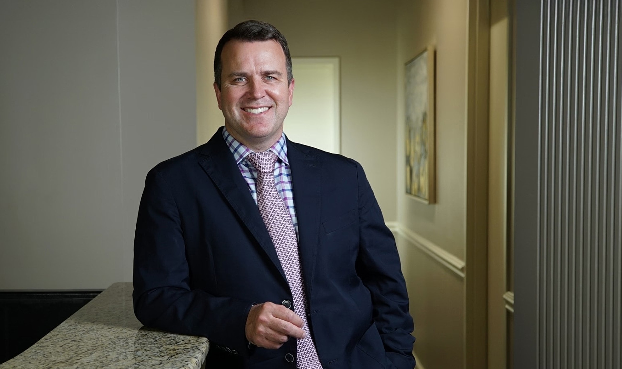 Smiling man in business attire leaning on counter.