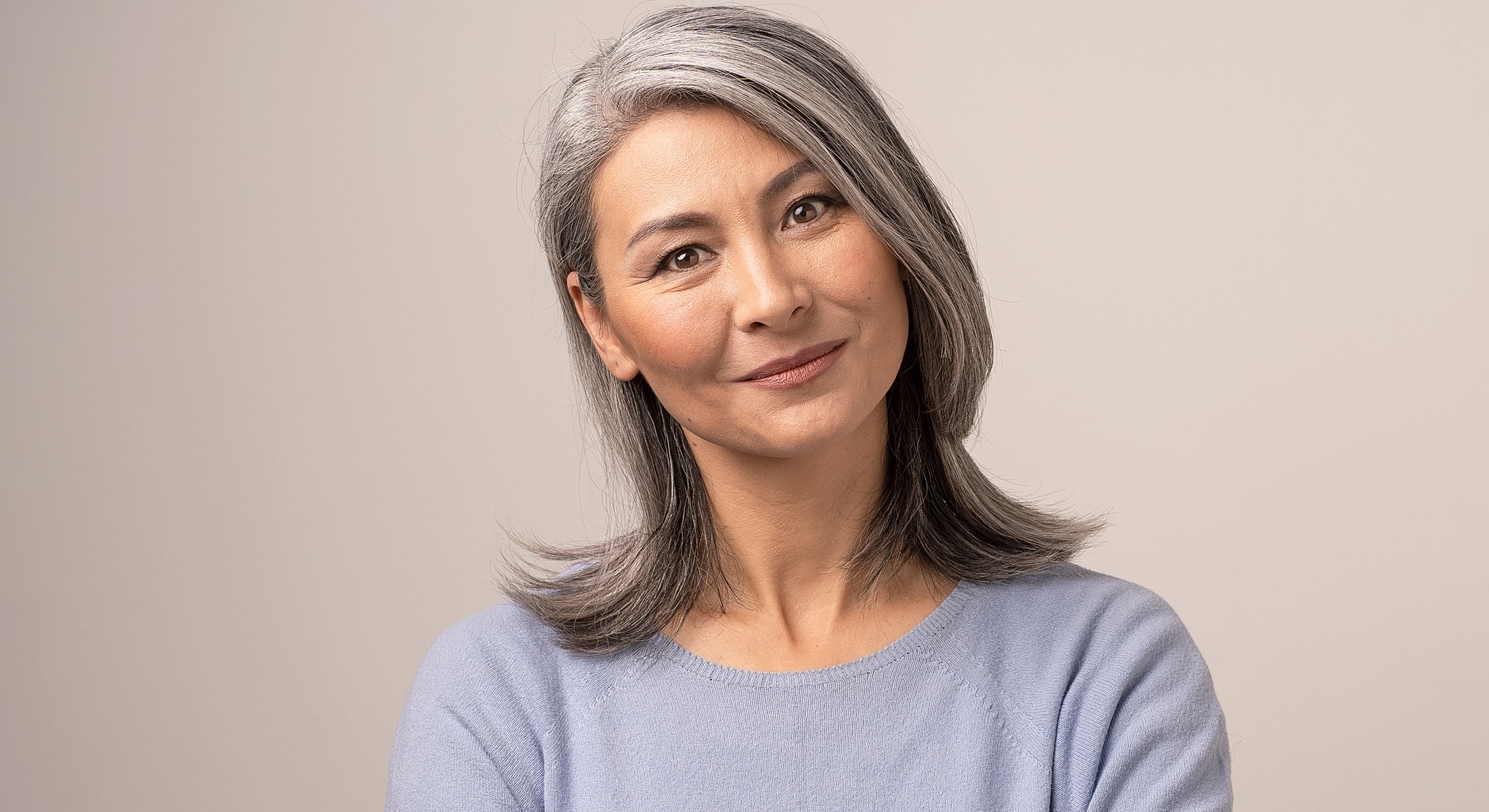 Smiling woman with gray hair wearing light sweater.