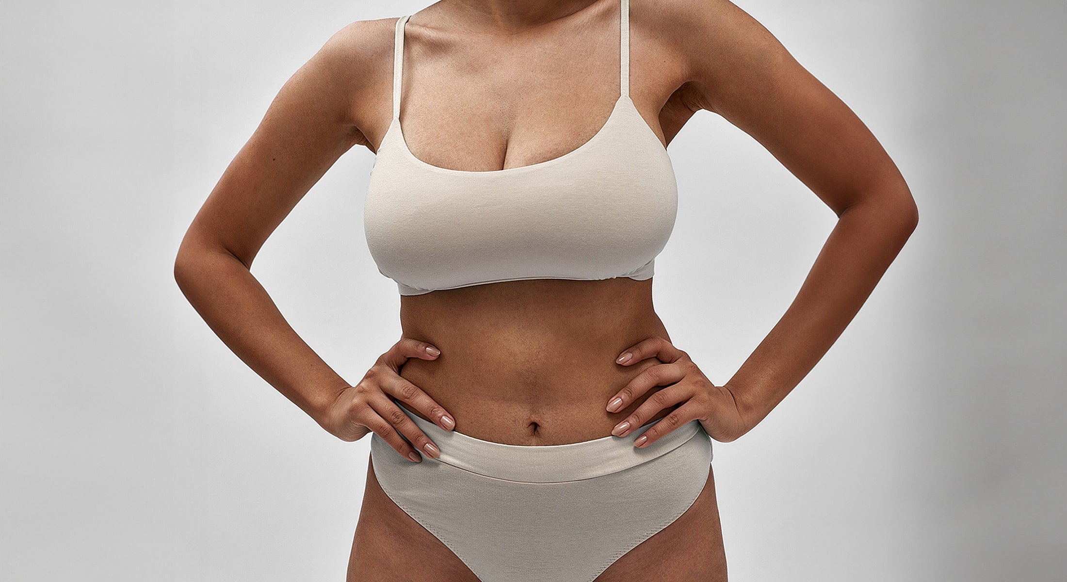 Model wearing neutral lingerie set, hands on hips.